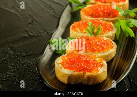Sandwiches mit frischem Weißbrot mit Butter und frischem roten Kaviar auf der schwarzen Schale, auf dem schwarzen Hintergrund Nahaufnahme. Stockfoto