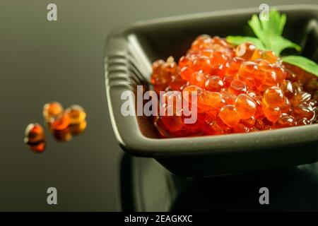 Frischer roter Kaviar in der schwarzen Schale auf dem schwarzen reflektierenden Hintergrund. Gesunde Meeresfrüchte, Luxus, lecker. Stockfoto