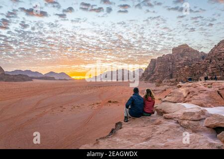 Ein junges Paar beobachtet bei Sonnenaufgang über wadi Rum Wüste in Jordanien Stockfoto