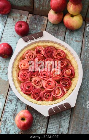 Roher Apfelrosenkuchen und Bio-Äpfel auf dem schäbigen blauen Tisch. Hausgemachtes gesundes Dessert Blick über den Kopf Stockfoto