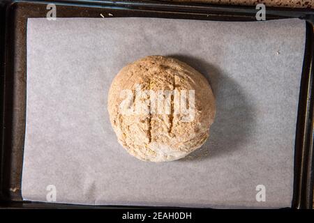 Eine Kugel Brotteig wird auf Pergamentpapier gelegt und bereit, in das Backpapier gelegt zu werden. Serie Schritt-für-Schritt Herstellung hausgemachtes Brot. Bild 1 Stockfoto