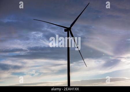 Silhouette Windturbine Offshore Windmühle aus Eisen mit Klingen Seitenansicht gegen einen blauen Himmel mit Wolken bei Sonnenuntergang, alternativer Strom Stockfoto