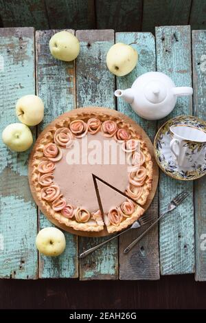 Hausgemachter Apfelrosenkuchen mit Sahne-Füllung serviert mit Bio-Äpfel und Tee auf blauem grobem Holz Hintergrund Overhead Anzeigen Stockfoto