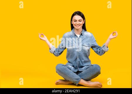 Ruhe bewahren. Foto einer zufriedenen ruhigen kaukasischen jungen Frau mit geschlossenen Augen, meditiert in Lotusposition auf isoliertem weißem Hintergrund Stockfoto