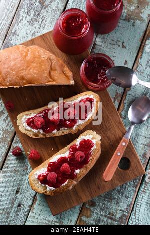 Hausgemachte Beerenmarmelade mit frischen Himbeeren und Johannisbeeren auf Ciabatta Toasts auf hölzernen Schneidbrettern Overhead Ansicht Stockfoto