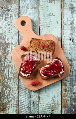 Hausgemachte Beerenmarmelade mit frischen Himbeeren und Johannisbeeren auf Roggen Brottoastes auf hölzernen Schneidebrettern Blick von oben Stockfoto