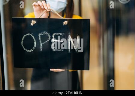 Nahaufnahme eines Schildes, DAS AM Eingang zu einem Restaurant oder Café geöffnet ist. Weibliche Hand hält Schild OFFEN am Eingang zu einem Restaurant, Bar, Café oder Shop Stockfoto