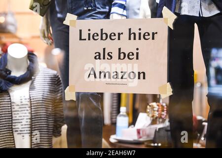 Berlin, Deutschland. Februar 2021, 09th. Am Fenster eines Modehaus in Friedrichshagen hängt ein Schild mit der Aufschrift "besser hier als bei Amazon". Außerdem sind viele Geschäfte wegen der Pandemie geschlossen. Quelle: Kira Hofmann/dpa-Zentralbild/dpa/Alamy Live News Stockfoto