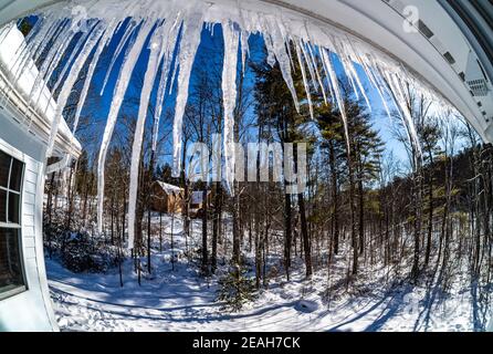 Connecticut, USA, 8. Februar 2021 - Eiskellen, die an einem verschneiten Wintertag gegen die aufgehende Sonne vom Dach eines Hauses hängen. Kredit: Enrique Shore/ Stockfoto