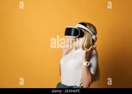 Junge blonde Frau in weißem T-Shirt und VR-Brille ist Erstaunt über etwas, das sie in der virtuellen Realität gesehen hat Stockfoto