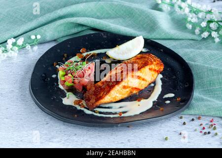 Portion gegrilltes Lachsfischsteak-Filet, Thunfischtartar auf schwarzem Teller Stockfoto