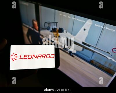 Person, die Mobiltelefon mit Logo der italienischen Verteidigungsfirma Leonardo S.p.A. auf dem Bildschirm vor der Business-Webseite hält. Fokus auf Handy-Display. Stockfoto