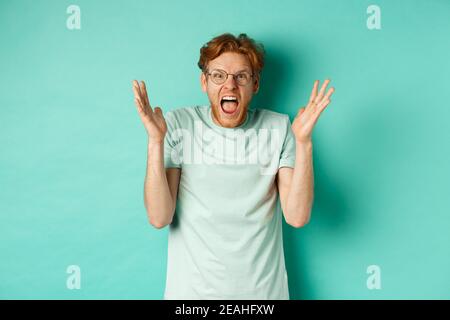 Porträt von verzweifelten und wütenden Rotschopf Kerl verlieren Temperament, schreien und Händeschütteln empört, starrte mit wütendem Gesicht auf die Kamera, stehen über Stockfoto