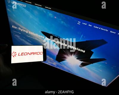 Hochwinkelansicht der Person, die Smartphone mit Logo der italienischen Verteidigungsfirma Leonardo S.p.A. auf dem Bildschirm mit Website hält. Fokus auf Handy-Display. Stockfoto