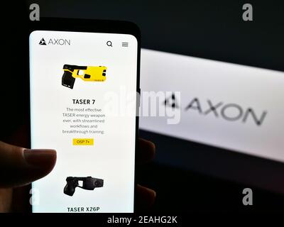 Person, die Mobiltelefon mit Produkt-Website des amerikanischen Waffenherstellers Axon Enterprise Inc. Auf dem Bildschirm mit Logo hält. Fokus auf der Mitte des Telefondisplays. Stockfoto