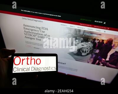 Person hält Smartphone mit Logo der amerikanischen Firma Ortho Clinical Diagnostics auf dem Bildschirm vor der Website. Konzentrieren Sie sich auf die Telefonanzeige. Stockfoto