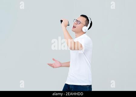 Junger asiatischer Mann mit Kopfhörern, der Musik vom Handy hört Telefon und Gesang isoliert auf hellgrauem Hintergrund Stockfoto