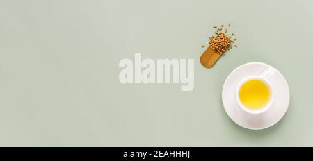 tasse Buchweizentee oder Kuqiaocha auf hellgrünem Hintergrund. Draufsicht auf gesunden Soba-Tee und Grütze im Löffel auf grünem Papier Hintergrund. Flach liegend. Speicherplatz kopieren. Langes horizontales Banner Stockfoto