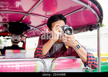 Junger asiatischer Tourist, der auf Reisen mit der Kamera fotografiert Auf lokalen Tuk Tuk Taxi in Bangkok Thailand Stockfoto