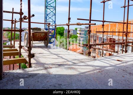 Gebrauchte industrielle veraltete Schubkarre auf Holzplattform über dem Gebäude platziert Standort als Teil des Gerüsts gegen Gebäude unter gelegt Konstruktion für Stockfoto