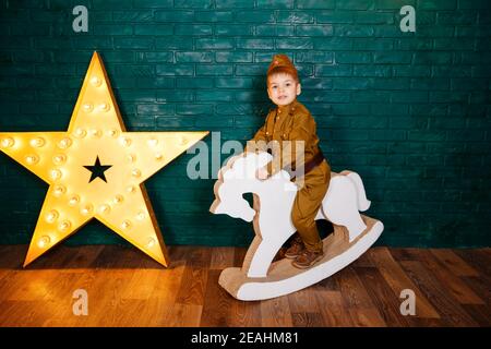 Kind in einem Anzug. Kind reitet weißes Pferd. Kinder spielen mit Spielzeug. Stockfoto