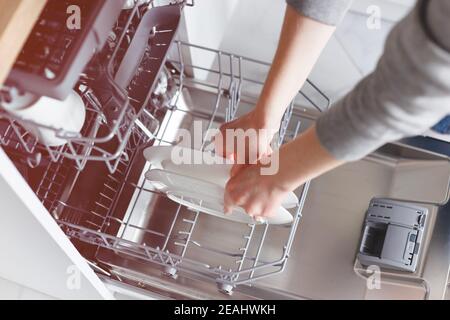 Nahaufnahme der weiblichen Hände, die das Geschirr in den Geschirrspüler geben. Stockfoto