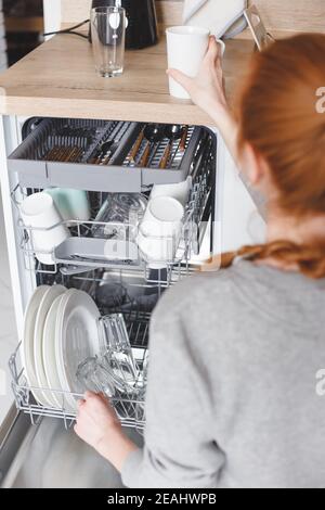Hausarbeit: junge Frau setzen Geschirr in der Spülmaschine Stockfoto