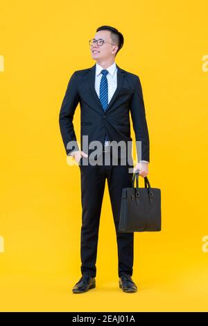 Glücklich zuversichtlich asiatischen Mann in fomral Business Anzug stehen und Der aufsteigende Kopf ist auf gelbem Hintergrund isoliert Stockfoto