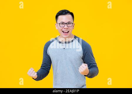 Portrait des begeisterten Siegers Asian Mann seine Fäuste mit Lächelndes Gesicht auf gelbem Hintergrund Stockfoto