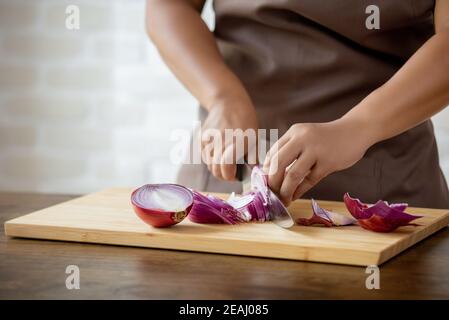 Nahaufnahme der Frau Hände schneiden rote Zwiebel auf braun Holzbrett in der heimischen Küche Stockfoto