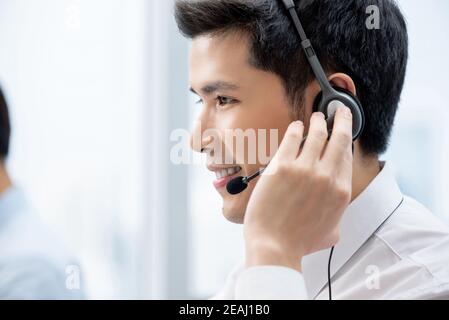 Lächelnd gut aussehende asiatische Mann arbeitet im Call Center Büro als Ein Kundendienstbetreiber Stockfoto