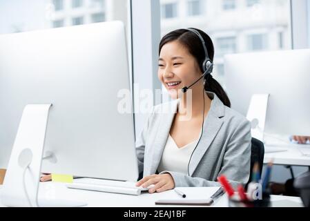 Lächelnd schöne asiatische Frau trägt Mikrofon-Headset arbeiten im Gespräch Center Office als Telemarketer Stockfoto