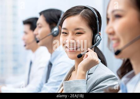 Lächelnd schöne asiatische Frau arbeitet im Call Center Büro mit Team als Kundendienstmitarbeiter Stockfoto