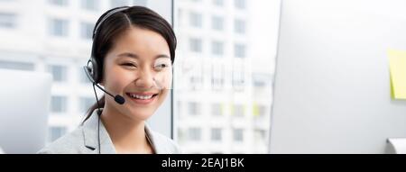 Lächelnde, schöne Asianerin, die als Kundendienst-Bedienerin im Callcenter-Büro arbeitet Stockfoto