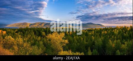 Schöne Landschaft mit Hügeln, umgeben von allen Seiten von einem Fluss, Wald und beleuchtet von den Strahlen der Morgensonne durch die Wolken. Stockfoto