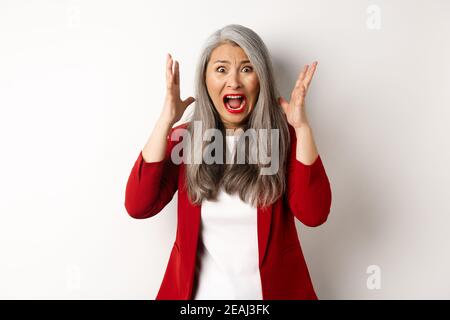 Asiatische Senior Geschäftsfrau schreien und schauen empört, fühlen sich beunruhigt und schreien, vor weißem Hintergrund stehen Stockfoto