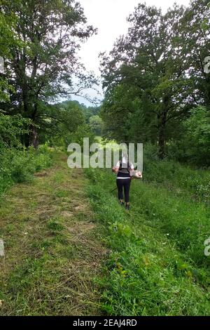 Junge Frau mäht das Gras mit einem Trimmer auf den abfallenden Hügeln in der Karpaten Region, ländliche Arbeit, Mähen der grass,2021 Stockfoto