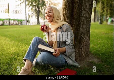 Arabisches Mädchen in Hijab hält Apfel und Lehrbuch Stockfoto