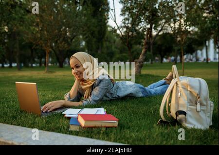 Arabische Studentin liegt auf dem Gras mit Laptop Stockfoto