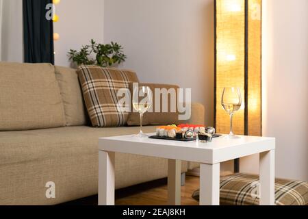 Ein Set aus farbenfrohem Sushi auf einem weißen Tisch mit Wein in einem gemütlichen Raum. Stockfoto