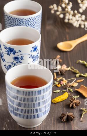 Nahaufnahme von drei blauen Tassen mit Tee, weißen Blumen und Holzlöffel, selektiver Fokus, auf Holztisch, vertikal Stockfoto