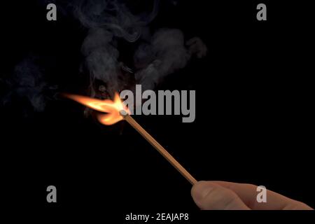 Hand hält ein brennendes Streichholz mit Feuerflamme und Rauch auf schwarzem Hintergrund. Stockfoto
