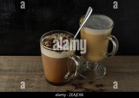 Zwei Glasplatten mit Cappuccino und Eisschokolade auf einem Holztisch mit schwarzem Strukturhintergrund. Selektiver Fokus. Stockfoto
