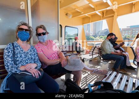 Jan 2021: Zwei Frauen lächeln durch ihre Gesichtsmasken, während sie auf einer Sydney Ferry den Hafen hinunter nach Manly in Australien fahren Stockfoto