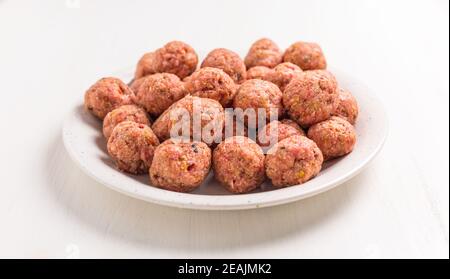 Rohe Fleischbällchen auf Teller und weißem Hintergrund Stockfoto