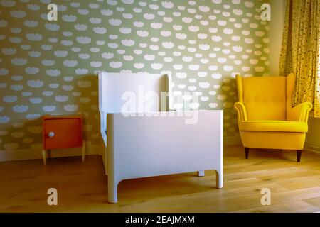 Schlafzimmer für Kleinkinder, mit Wolkenmuster an der Wand, Vintage-Stuhl, Holzboden und orangefarbenem Nachttisch. Stockfoto