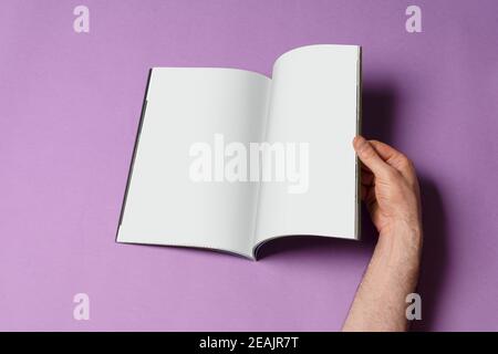 Männliche Hand öffnete einen Buch-Katalog auf lila Hintergrund Mock-up-Serie 260 Stockfoto