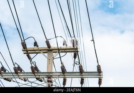 Dreiphasiger elektrischer Strom für die Übertragung von Strom durch elektrische Netze. Elektrische Energie für die Unterstützung der Fertigungsindustrie. Hochspannungsmasten und Drahtseilen gegen blauen Himmel und weiße Wolken. Stockfoto