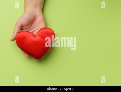 Weibliche Hand hält rote Textil Herz, grüner Hintergrund Stockfoto