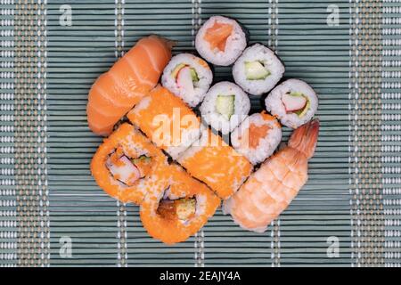 Traditionelles japanisches Sushi-Menü. Nahaufnahme verschiedener Sushi-Brötchen mit Lachs, Sashimi und anderen Scheiben rohen Fischs auf einer grünen Bambusmatte. Makro. Draufsicht. Stockfoto